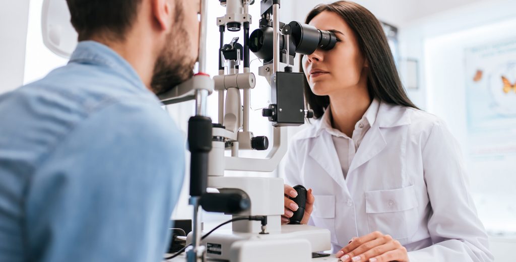 Attractive female doctor  ophthalmologist is checking the eye vision of handsome young man in modern clinic. Doctor and patient in ophthalmology clinic.
